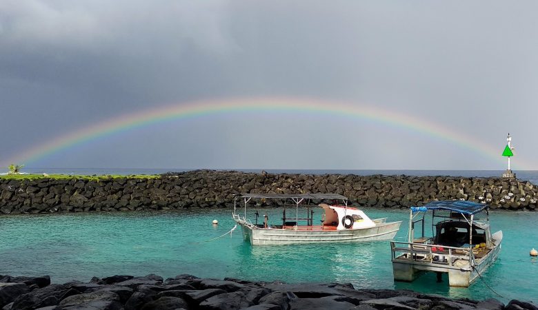 Full rainbow cast over two boats in a harbor.