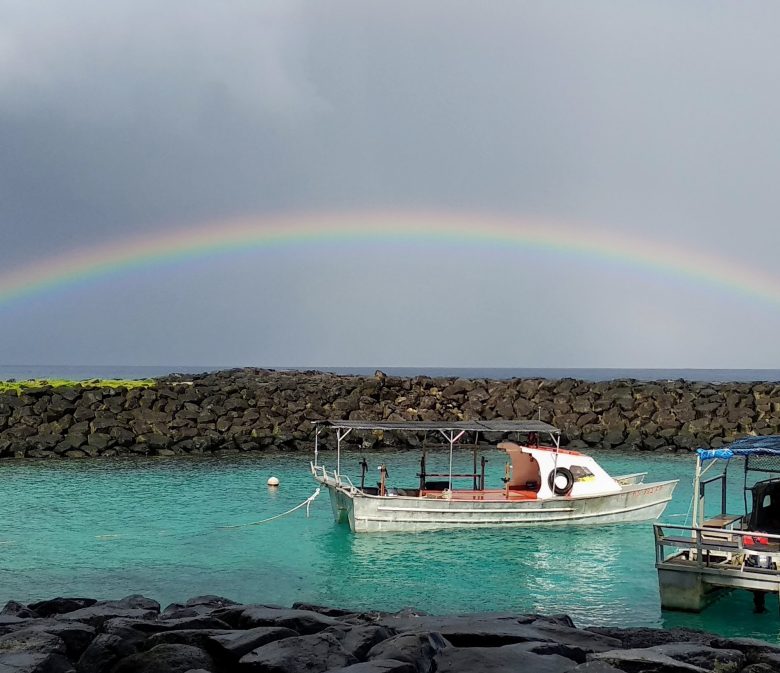 Full rainbow cast over two boats in a harbor.